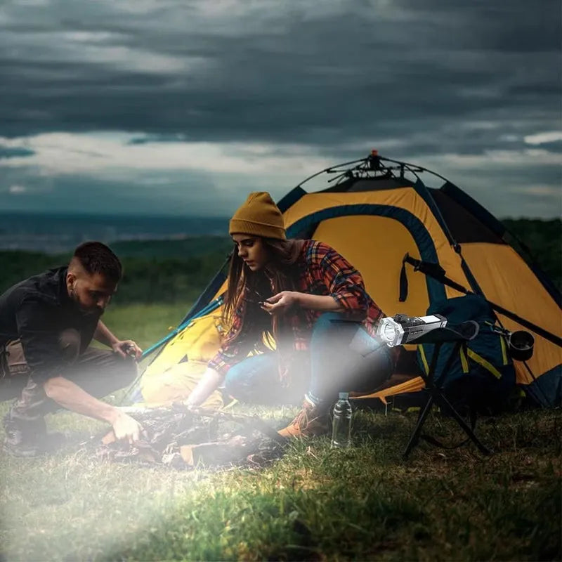 Rechargeable torch lit near camping tent while people set up gear.