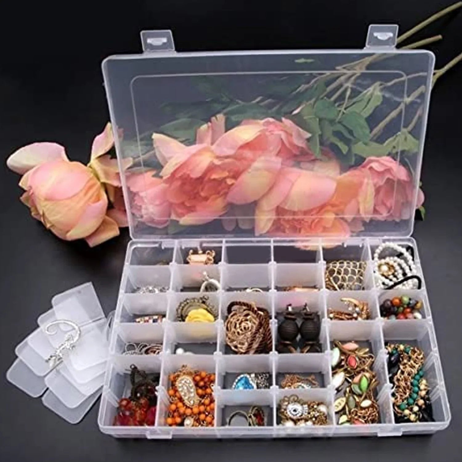 Clear plastic jewelry organizer box with adjustable compartments, open lid, visible rings and beads
