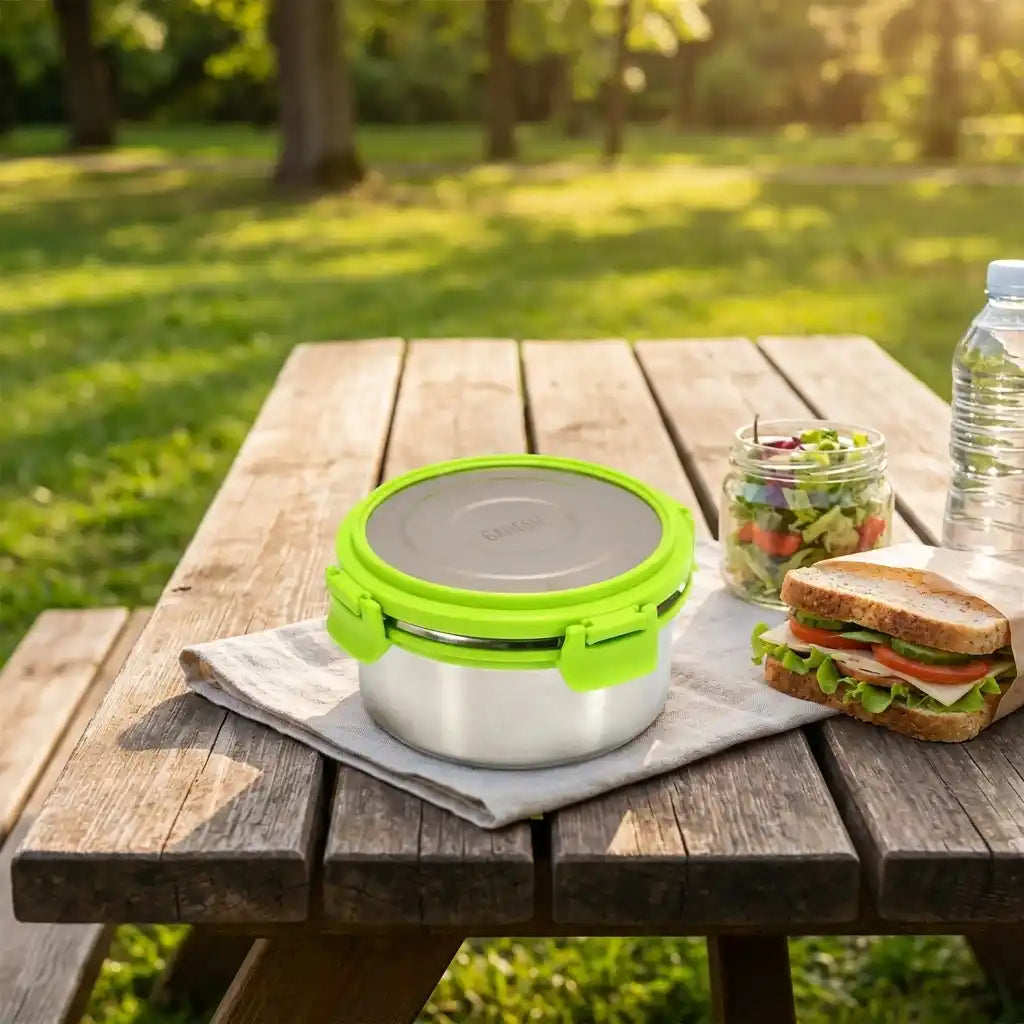 Stainless-steel round lunch box with bright green lid, closed on table.