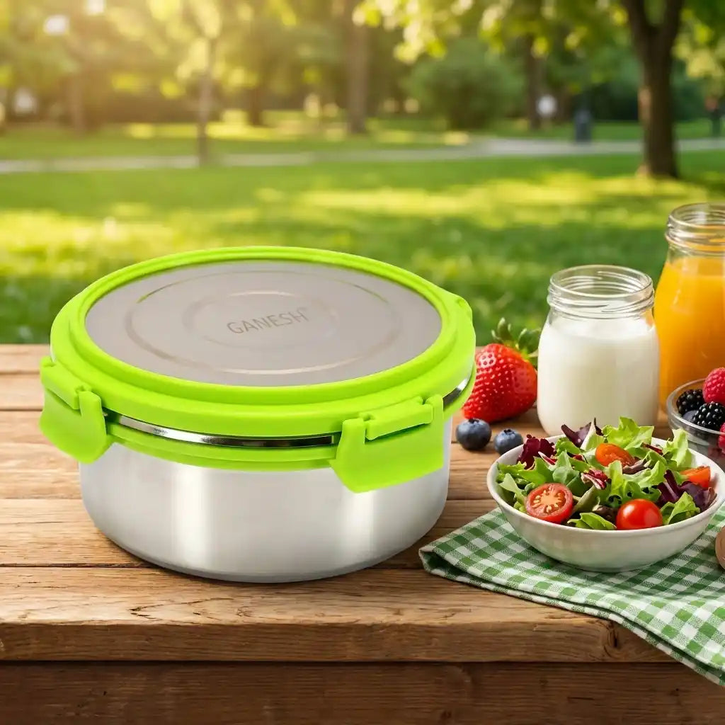 Round stainless-steel lunch box with bright green lid, closed on table with fruit.