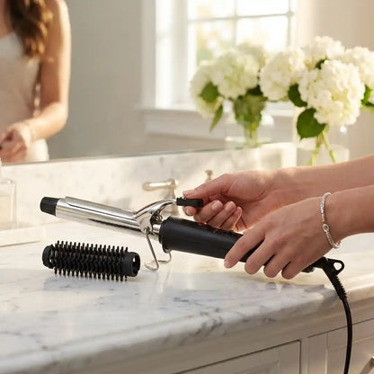 Hair curling iron in hand with black grip and chrome barrel with roller comb