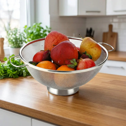 Stainless steel colander with two side handles, holding mixed fruit over counter