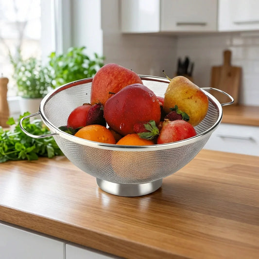 Stainless steel colander with two side handles, holding mixed fruit over counter
