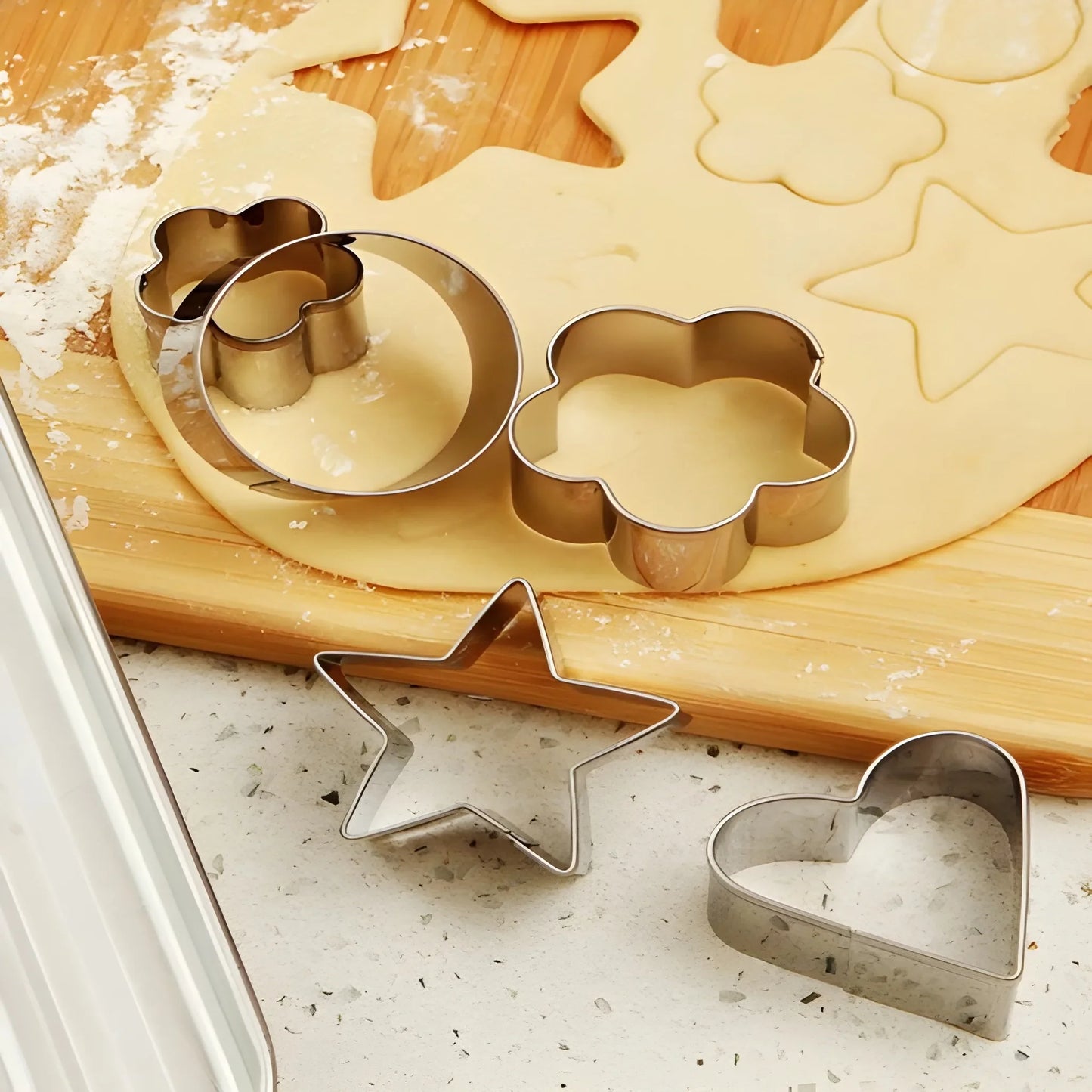Stainless cookie cutter set with star, heart, and tree shapes on dough