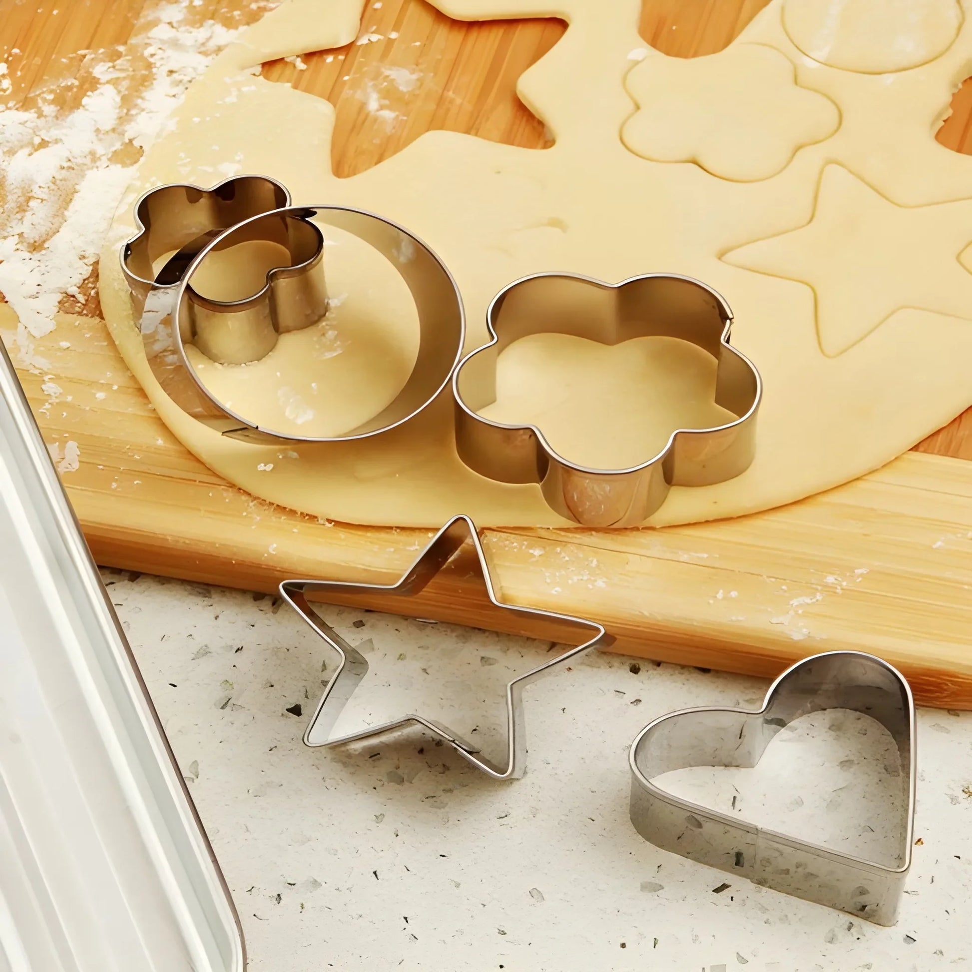 Stainless cookie cutter set with star, heart, and tree shapes on dough