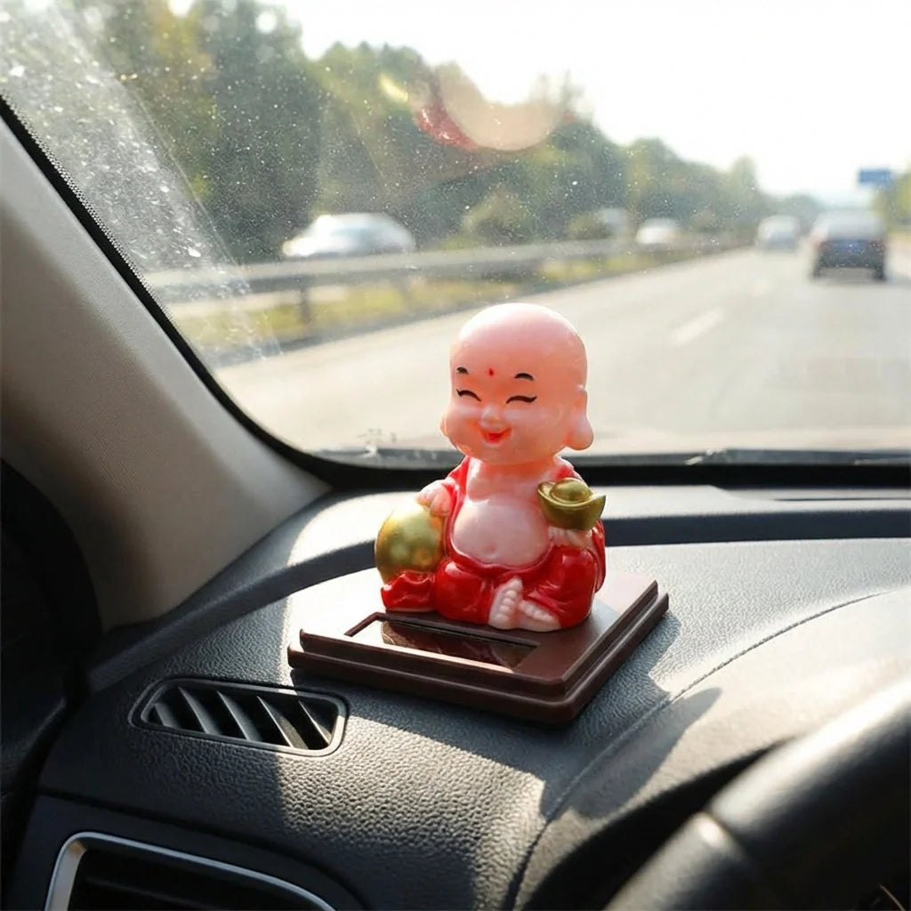 Solar-powered Buddha statue on dashboard, red robe and gold details