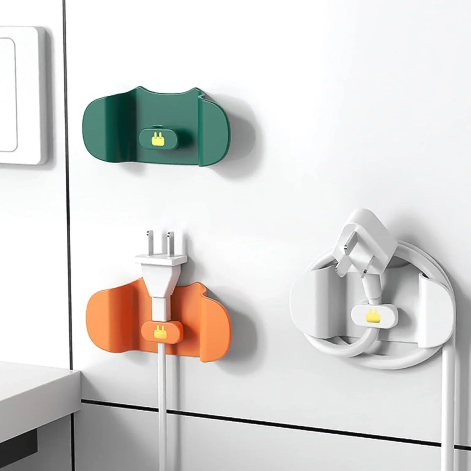 Wall plug holder clips mounted on wall, green and orange with plug openings